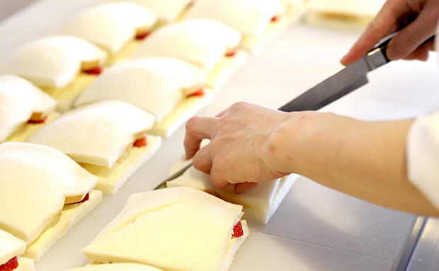 調理写真:サンドイッチをまな板の上に乗せ、包丁で切っているシーン